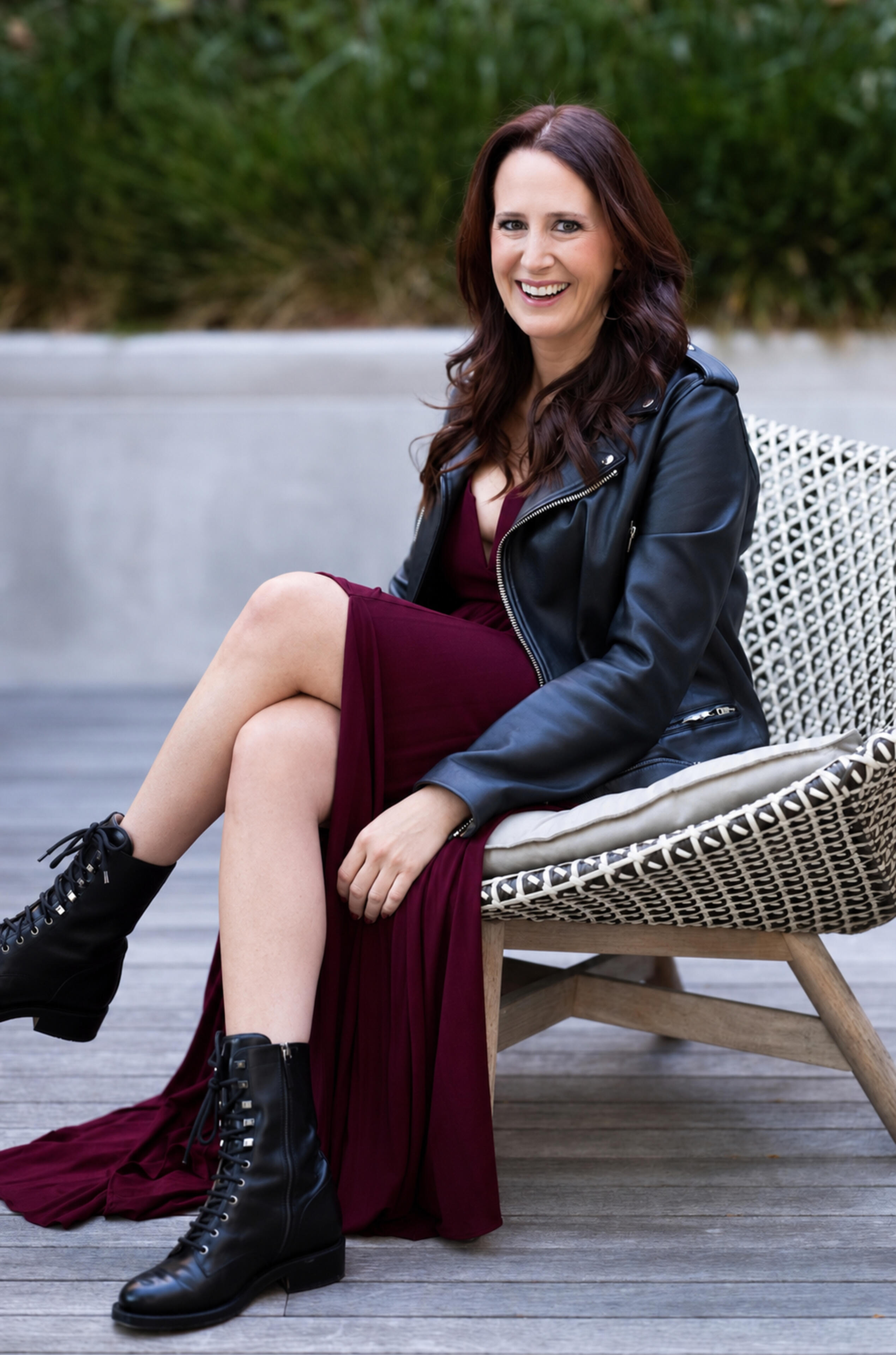 Tracy Weiss seated outdoors in a burgundy dress and leather jacket